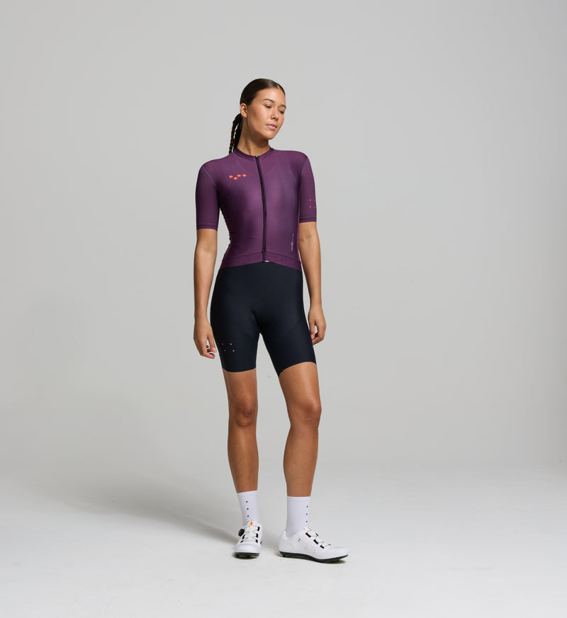 Front view of female cyclist in aubergine Classic Jersey – form-fitting cut with low collar, extended sleeves, and breathable side panels for warm-weather airflow.