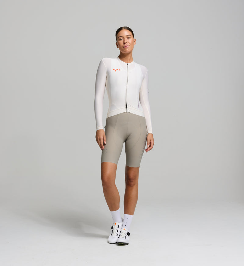 Front view of female cyclist in almond Classic Long Sleeve Jersey – sleek, performance-focused fit with extended sleeves and low collar for cool-weather versatility.