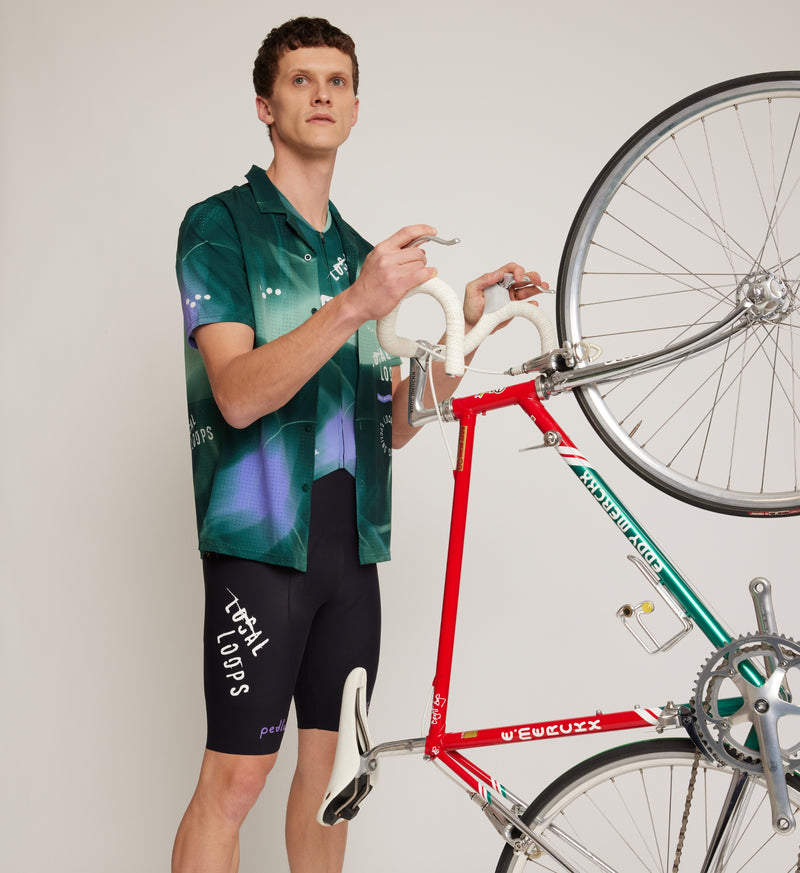 Front view of model wearing LOCAL LOOPS Unisex Beach Shirt in Race Pine, showcasing a short-sleeved, button-up design with a casual camp collar and breathable perforated fabric for style and comfort during post-ride gatherings.