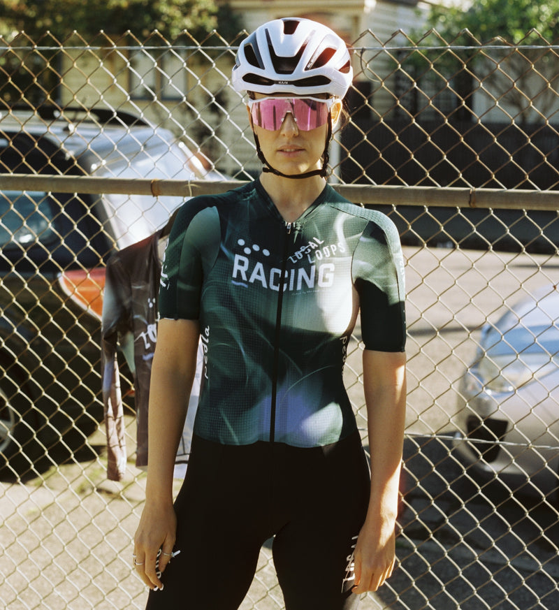 Front view of model wearing LOCAL LOOPS Women's Pro Pursuit Crit Suit in Race Team, showcasing a race-fit design with next-to-skin stretch-woven fabrics, low-cut race collar, and bonded cuffs for streamlined performance and comfort during high-speed rides.