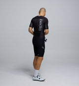 Side profile of the Men's Pro Pursuit Crit Suit – Black, showing sculpted sleeve panels with AeroPRISMA fabric, silicone leg grippers, and ergonomic design for high-speed movement.