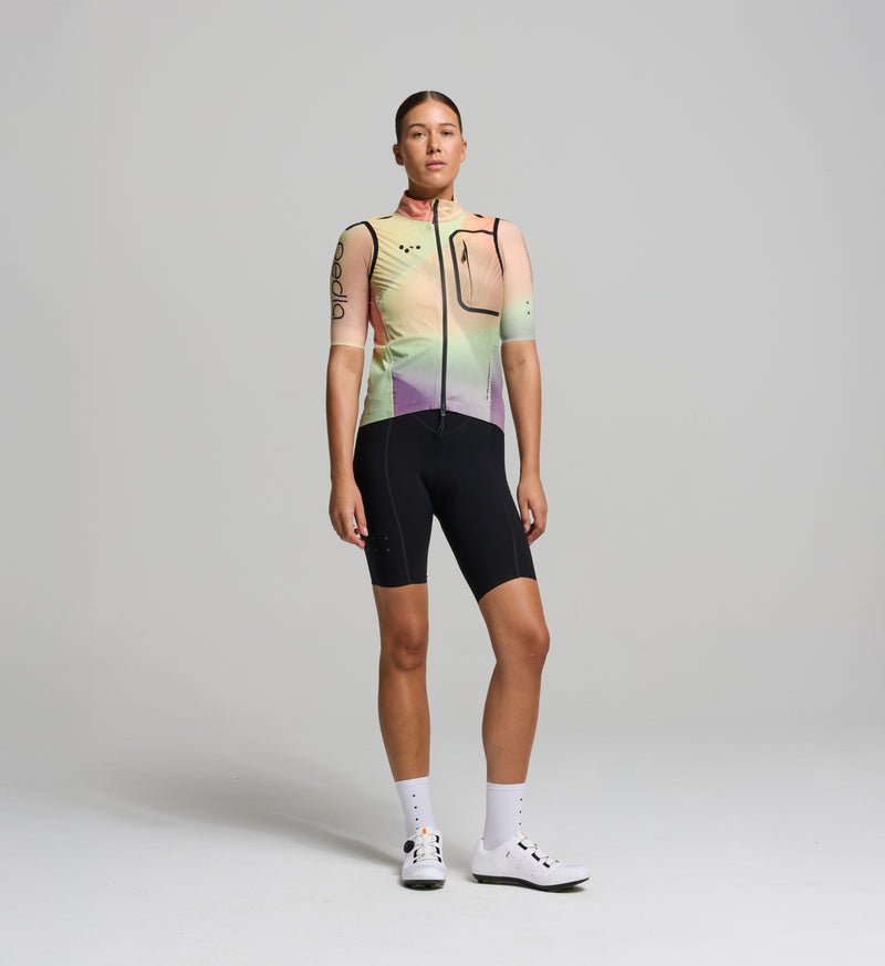 Cyclist wearing the Women’s Pro Deflect 2.0 Cycling Gilet in Peach, showcasing its streamlined fit, high stand collar, and breathable fabric.
