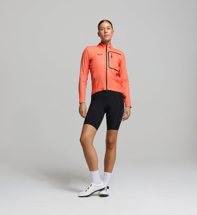 Cyclist wearing the Women’s Pro Deflect 2.0 Cycling Jacket in Apricot, showcasing its high stand collar, streamlined fit, and breathable waterproof fabric.
