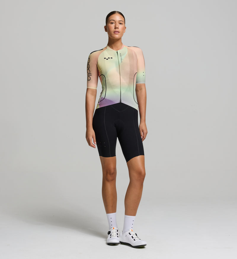 Cyclist wearing the Women’s Pro Pursuit 2.0 Cycling Jersey in Motion Peach, highlighting its sleek aero fit, breathable Italian fabric, and streamlined design.