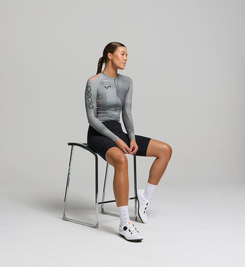 Cyclist wearing the Women’s Pursuit LS 2.0 Cycling Jersey in Motion Graphite, highlighting its aero fit, moisture-wicking Italian fabric, and sleek long sleeve design.