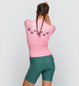 Back view of Essentials Women's Air Cycling Jersey in Flamingo on model, featuring a lightweight back pocket design, ventilated fabric for airflow, and rear reflective accents for visibility and safety on twilight rides.