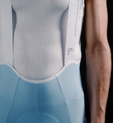 Close-up of men's Pedla SuperFIT 2.0 powder blue full-length cycling bib tights with white breathable mesh bib, Elastic Interface chamois, reflective logos, ergonomic seams and premium Italian fabric for aerodynamic support