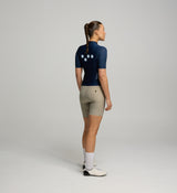 Woman wearing a navy cycling jersey and beige shorts on a plain background