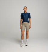 Women wearing a navy cycling jersey and beige shorts on a gray background