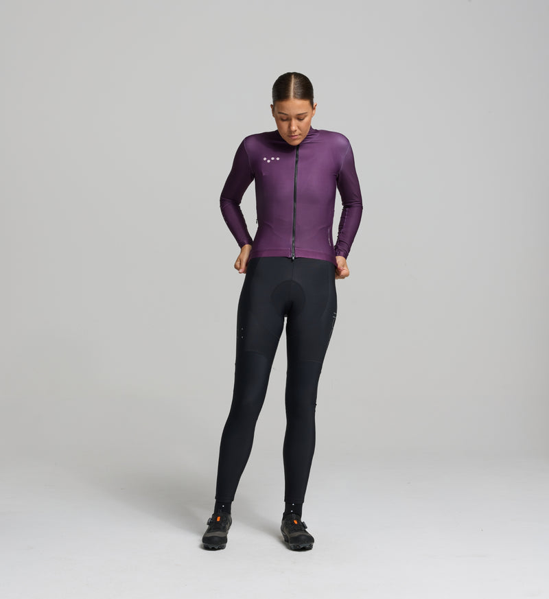 Female cyclist in aubergine thermal jersey – contoured front fit with articulated sleeves, designed for warmth, comfort, and movement during cool-to-cold rides.