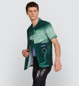 Side view of LOCAL LOOPS Unisex Beach Shirt in Race Pine on model, highlighting the relaxed fit, side slits for enhanced mobility, and distinctive Local Loops print that represents the inclusive spirit of the cycling community.