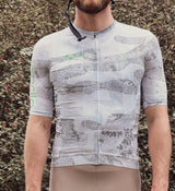 Close-up view of the NatureCAMO Men's Cycling Jersey in Sketch White on model, detailing the REPREVE® recycled fabric, UPF/SPF 30+ sun protection, and moisture-wicking properties that provide comfort and performance during cycling.