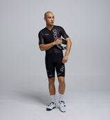 Front-facing image of a male cyclist wearing the Pro Pursuit Crit Suit in Black, highlighting the close-fitting aero cut, low-profile collar, and breathable woven fabric designed for speed.