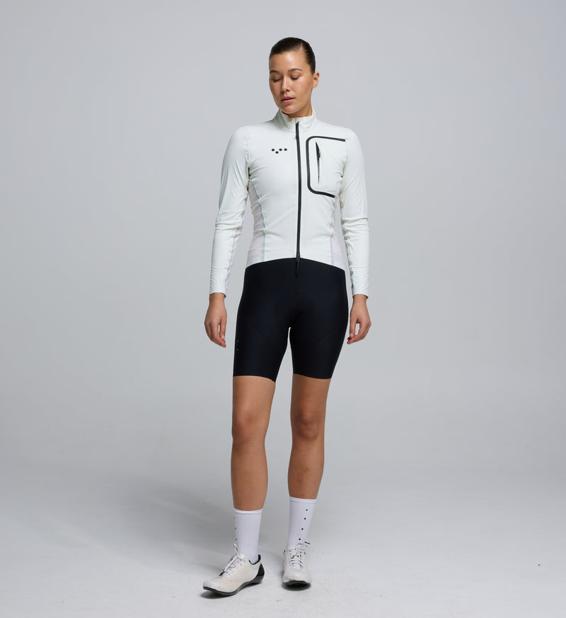 Front view of a female cyclist wearing the Porcelain Deflect 2.0 Jacket, featuring a high-performance fit, chest pocket with waterproof zipper, and clean, aerodynamic styling.
