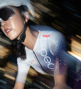 Front-facing image of a female cyclist wearing the AirFoils White Crit Suit, showing its sculpted race fit, low-cut collar, and aerodynamic woven sleeves built for high-performance rides.
