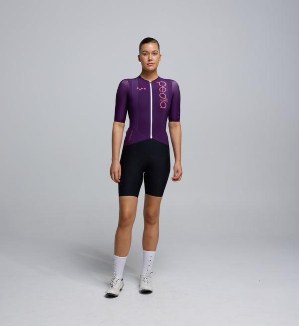 Front view of a female cyclist wearing the Plum Pursuit AIR Jersey, showing a close-fit silhouette, lightweight construction, and streamlined design for warm-weather performance.