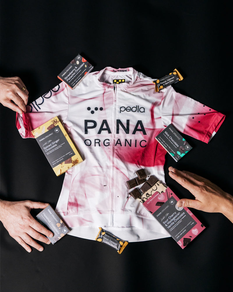 Pedla x Pana Organic white-and-pink team cycling jersey with limited-edition organic, plant-based vegan chocolate bars and crunchy hazelnut spread — sour cherry & Madagascan vanilla, pistachio, mint, spiced ginger, peanut caramel; artisanal cycling gift bundle, perfect gift for cyclists (total retail $280)