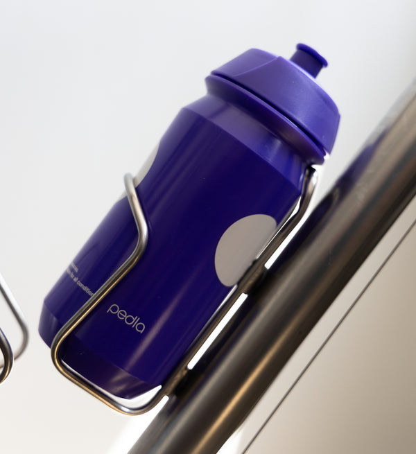 Purple Pedla bidon securely mounted in bike bottle cage; compact, accessible, and perfect for hydration on the move