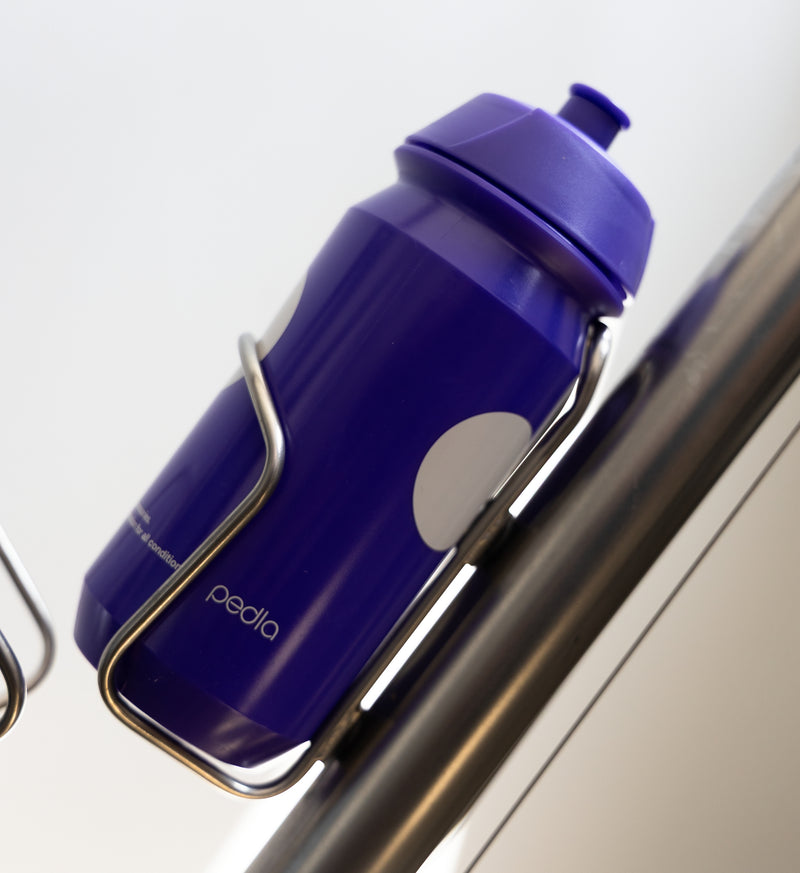 Purple Pedla bidon securely mounted in bike bottle cage; compact, accessible, and perfect for hydration on the move